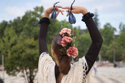 Portrait of young teenage girl in black dance dress, white shawl and pink carnations in her hair, dancing flamenco with castanets in her hands. Concept of flamenco, dance, art, typical Spanish dance.