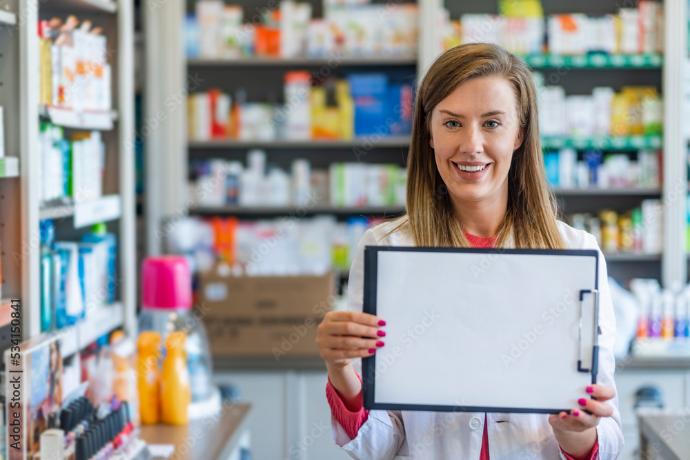 Beautiful smiling intern, who is holding the clipboard with empty paper. Woman is wearing white uniform, stands on a light white background. Clipboard with blank sheet in hands of female pharmacist Beautiful smiling intern, who is holding the clipboard with empty paper. Woman is wearing white uniform, stands on a light white background. Clipboard with blank sheet in hands of female pharmacist