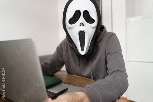 Anonymus person with ghost mask working with laptop. Halloween work concept