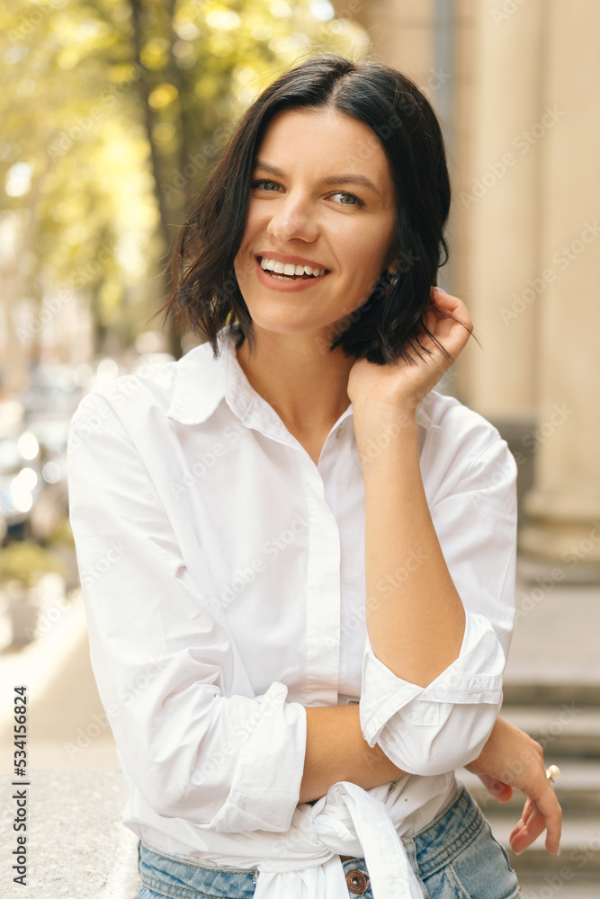 Vertical portrait of young smiling woman looking at the camera near city streets background. Vertical portrait of young smiling woman looking at the camera near city streets background.