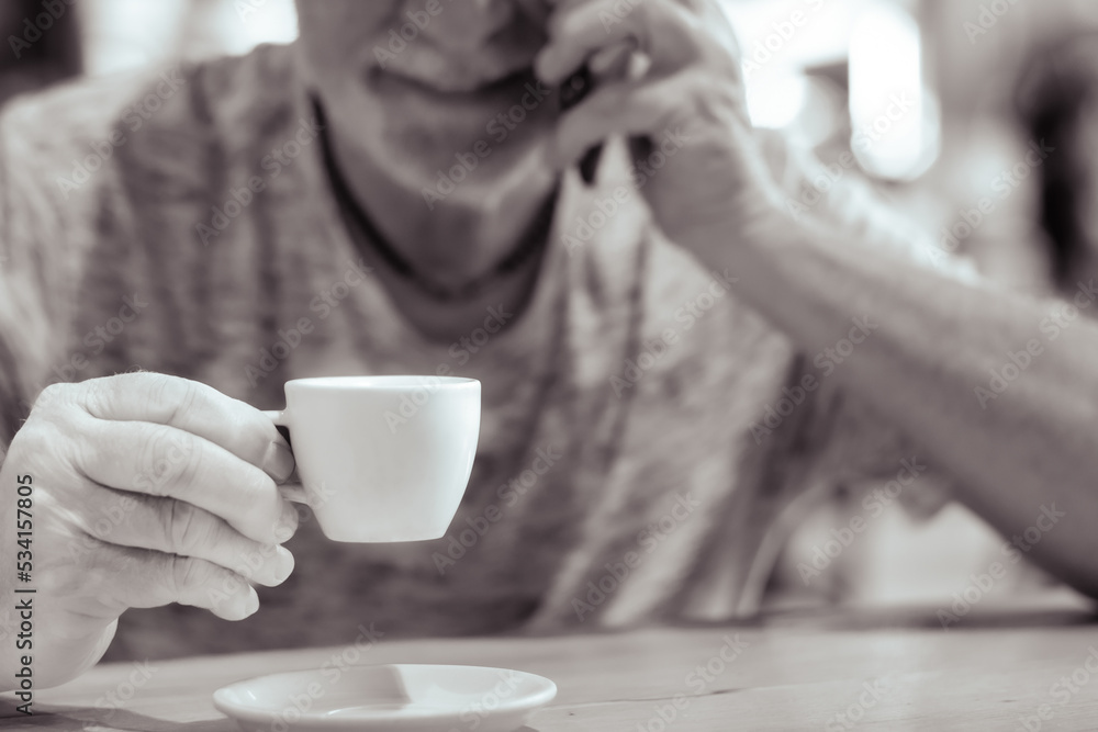 Cropped shot of defocused senior man talking on mobile phone while drinking coffee at cafeteria. Man using a smart phone while drinking espresso coffee Cropped shot of defocused senior man talking on mobile phone while drinking coffee at cafeteria. Man using a smart phone while drinking espresso coffee