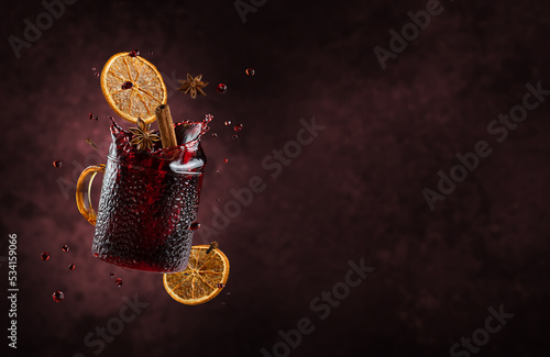 Mulled wine with splashes and flying ingredients on dark background. Copy space photo