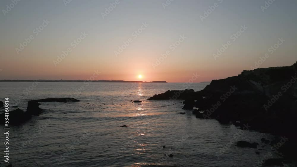 backward drone shot at the beach through two stones at sunset.