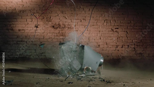 an old tube TV breaks on a concrete floor against a brick wall
