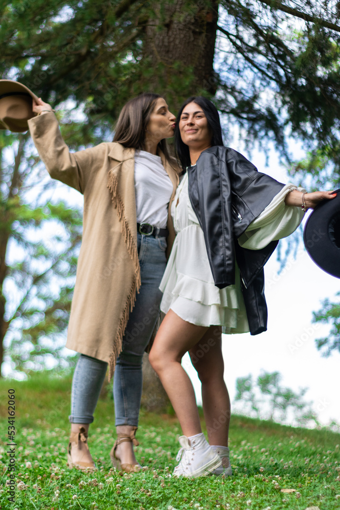 Lifestyle of two girls with hats kissing each other on the cheek in the ...