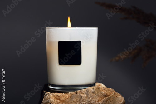 Burning candle in glass holder with space for logo on dark background closeup. Easy aromatherapy for everyday. Elegant home decor