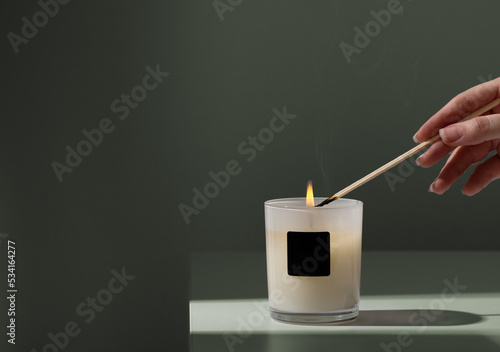 Obraz na płótnie Woman lights candle in glass holder with wooden skewer on green background closeup. Candlelight creating cozy atmosphere at home. Copy space w salonie