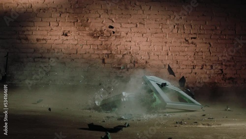 an old tube TV breaks on a concrete floor against a brick wall