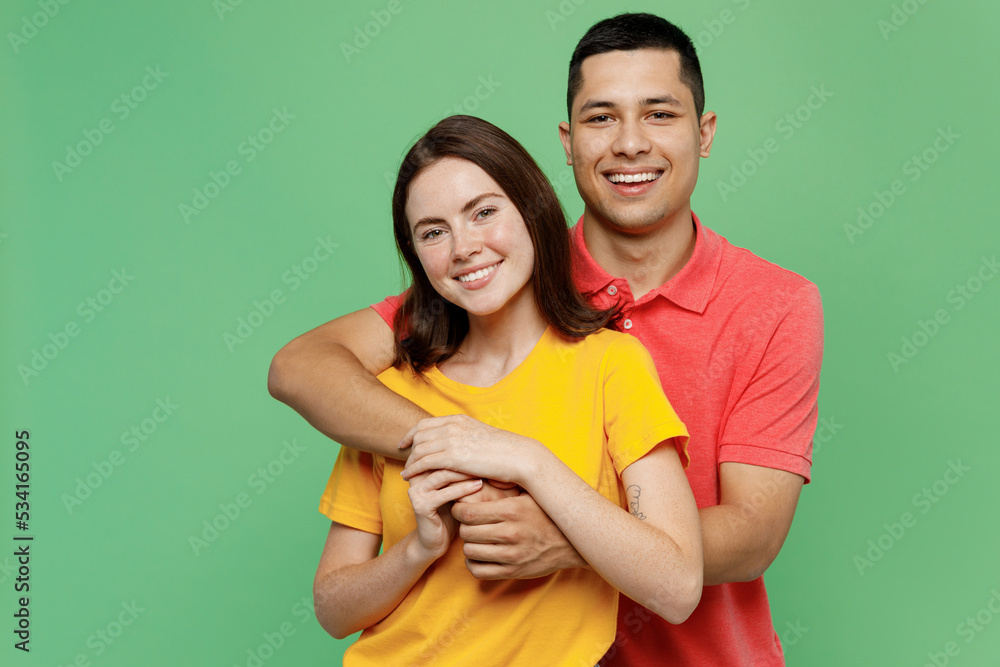 Fototapeta premium Young cheerful fun happy adorable couple two friends family man woman 20s wear basic t-shirts together boyfriend hug girlfriend isolated on pastel plain light green color background studio portrait