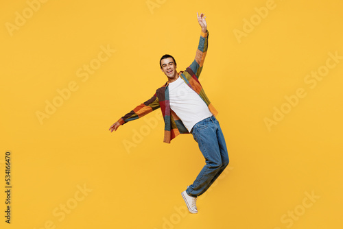 Full body young middle eastern man 20s he wear casual shirt white t-shirt look camera with outstretched hands dance stand on toes isolated on plain yellow background studio People lifestyle concept.