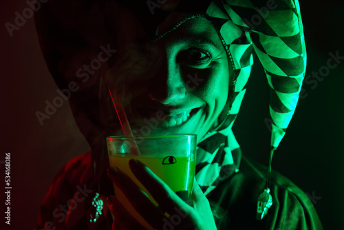 Woman dressed as a harlequin smiling holding a drink with smoke at a costume Halloween party. photo