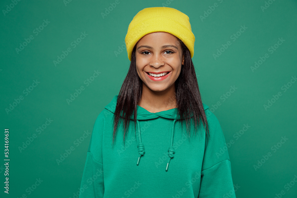 Little smiling happy fun kid teen girl of African American ethnicity 13-14 years old wear casual sweatshirt yellow hat look camera isolated on plain green background studio portrait Childhood concept.