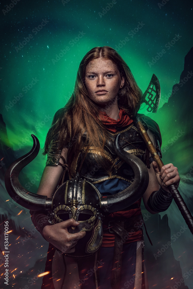 Obraz premium Shot of female warrior with helmet and axe dressed in armor against polar lights.