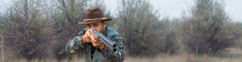Fototapeta premium Hunter man in camouflage with a gun during the hunt in search of wild birds or game.