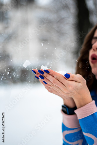girl in winter holds snow on her palms and blows on it, it's snowing