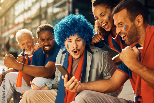 Canvas Print Group of passionate sports fans cheering while watching soccer match on mobile phone