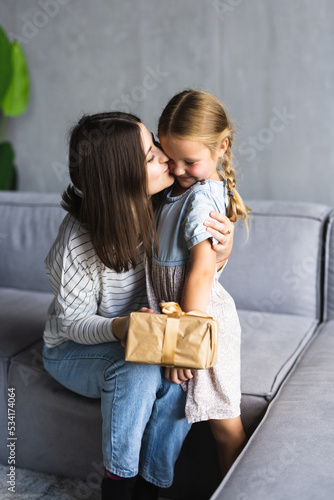 Cute little girl greeting her mother with present at home. Mother's day concept