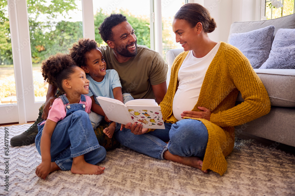 Army Family With Pregnant Mother Sitting On Floor In Lounge At Home Reading Book Together Army Family With Pregnant Mother Sitting On Floor In Lounge At Home Reading Book Together