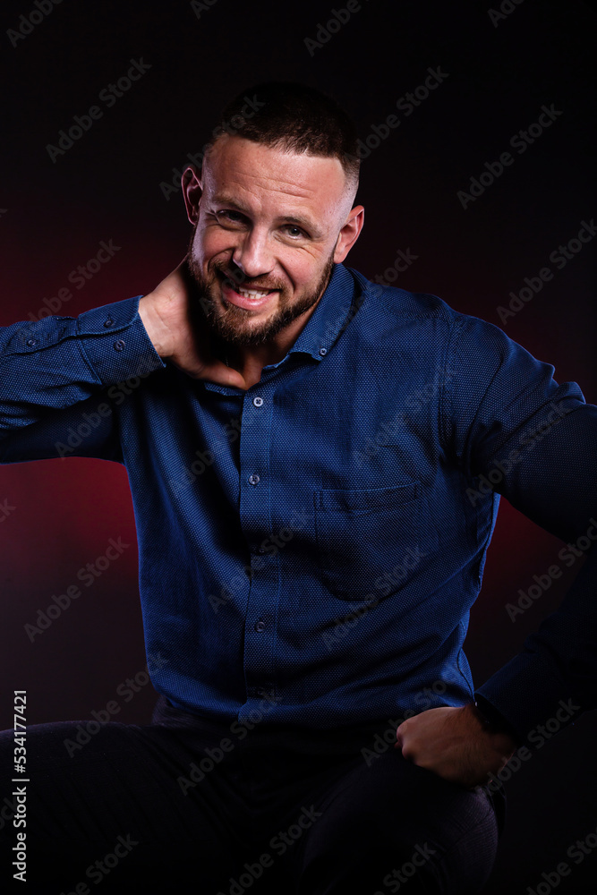 © oleg_ermak - Surprised and glad man in blue shirt, hold hands on his head. Handsome Posing in studio on dark red background