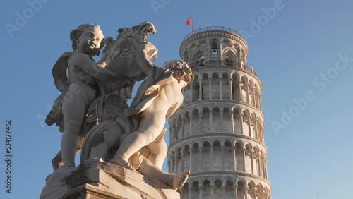close up of the Leaning tower of pisa with clear blue sky in the morning during golden hour with statue in the foreground filmed with a gimbal and a dolly movement in tuscany, italy photo