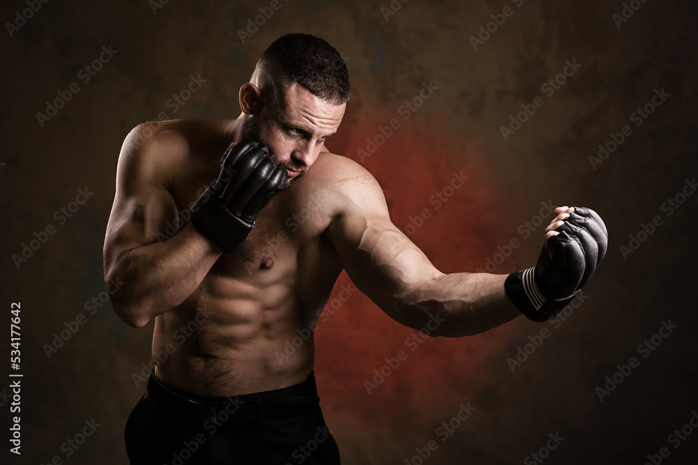 Studio portrait of fighting muscular man in black fighting gloves posing on dark background. The concept of mixed martial arts. Brutal bodybuilder energy and power boxing.
