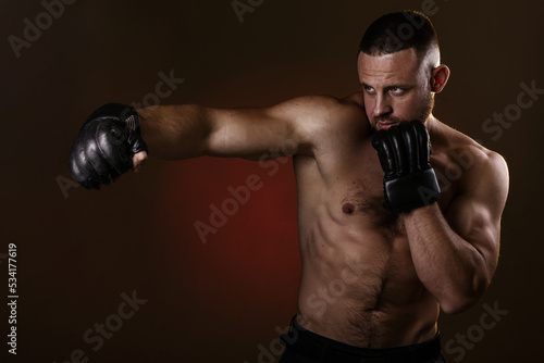 Studio portrait of fighting muscular man in black fighting gloves posing on dark background. The concept of mixed martial arts. Brutal bodybuilder energy and power boxing. © oleg_ermak