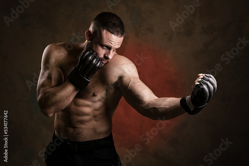 Studio portrait of fighting muscular man in black fighting gloves posing on dark background. The concept of mixed martial arts. Brutal bodybuilder energy and power boxing. © oleg_ermak