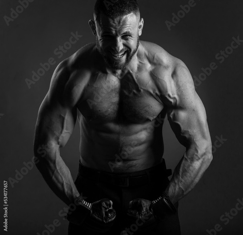 Studio portrait of fighting muscular man in black fighting gloves posing on dark background. The concept of mixed martial arts. Brutal bodybuilder energy and power boxing.
