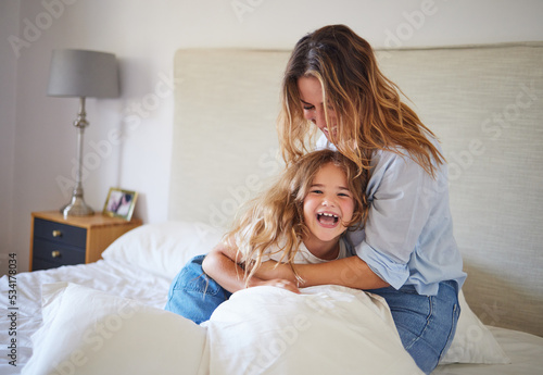 Mom and child on the bed playing together, having fun and laughing. Portrait of mother and daughter in bedroom, smiling while woman tickle young girl. Family, love and laughter in morning at home photo