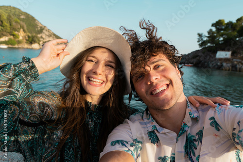 Successful traveling couple in love taking a selfie on a sunny summer day. Pretty girl and her handsome boyfriend with b having fun, laughing with the sea at the background. © Marijana