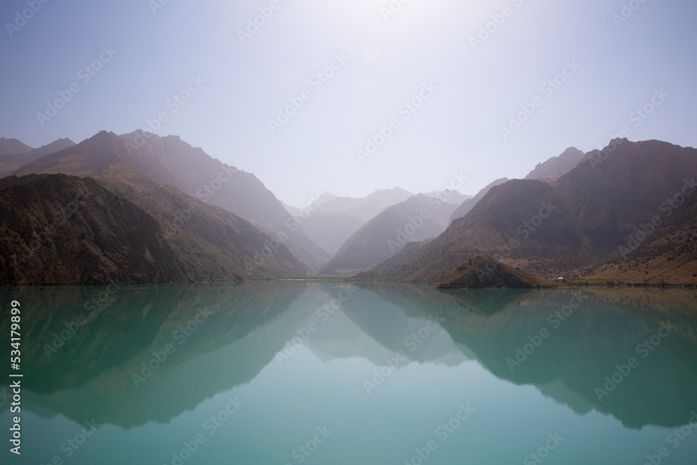 Top quality from canon r6 precisely focused showing reality,Iskanderkul lake in misty weather with  haze  above mountains showing more than 20 arches all reflected in the water of lake in Tajikistan