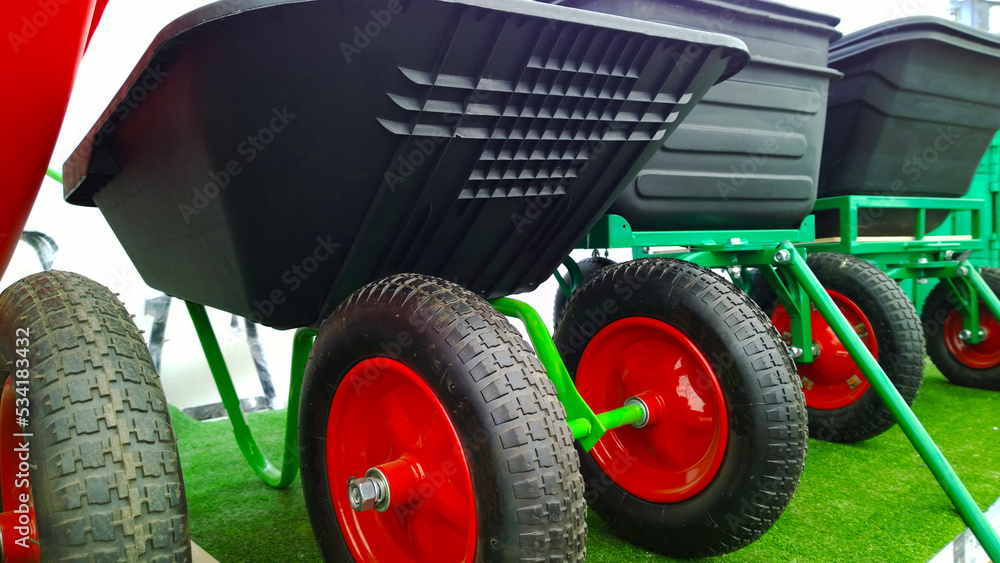 Naklejka premium Wheelbarrow in supermarket for sale. Hypermarket for gardeners. Wheel on green artificial grass. Gardening. Agricultural machinery. Equipment for construction industry. Garden trolley. Cart.