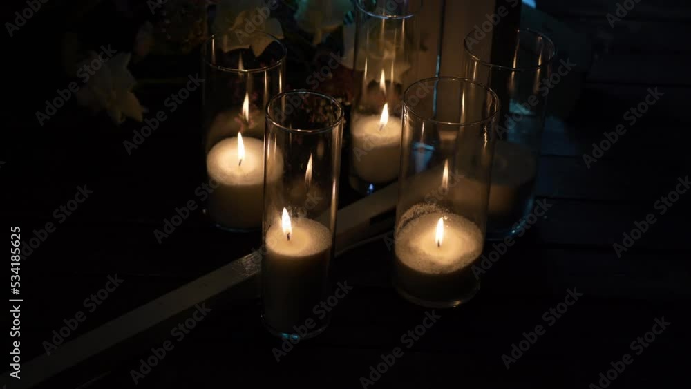 Burning white candles in a glass bulb stand wooden terrace of country hotel decorated with wedding bouquets at romantic evening Burning white candles in a glass bulb stand wooden terrace of country hotel decorated with wedding bouquets at romantic evening