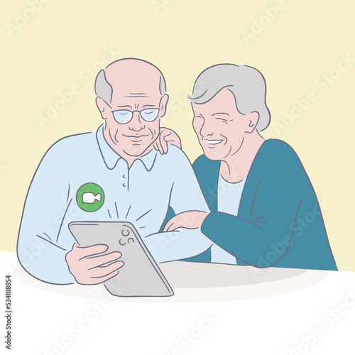 Smiling old married couple hugging and doing video call. Old man and old lady sit at a table and makes a video call using a tablet. Happy grandmother hugs husband and looks at the tablet screen