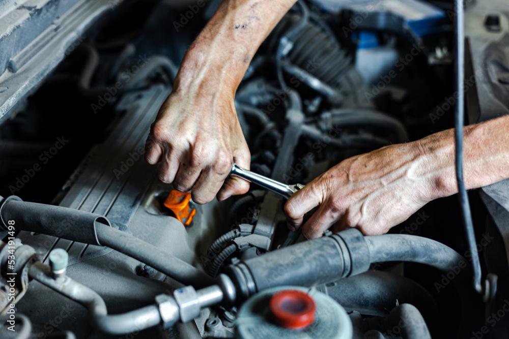 An auto mechanic works with a car engine in the mechanics' garage. Car repair close-up. An authentic close-up shot of an auto mechanic's hands. An auto mechanic works with a car engine in the mechanics' garage. Car repair close-up. An authentic close-up shot of an auto mechanic's hands.