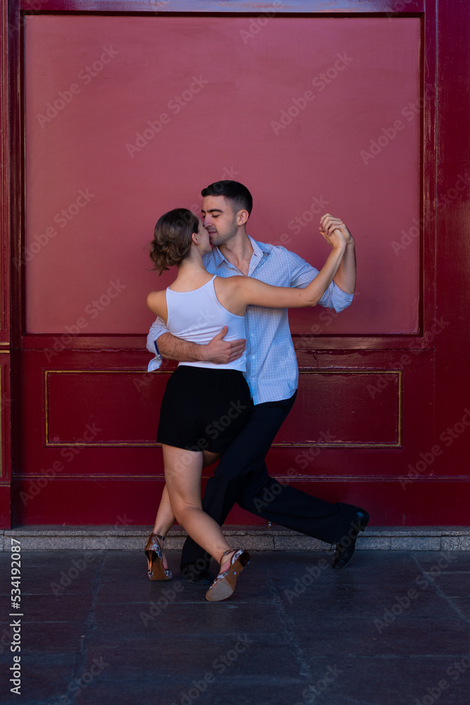 Boy in a suit and girl in shorts and a white t-shirt Couple dancing Tango, with a red background.