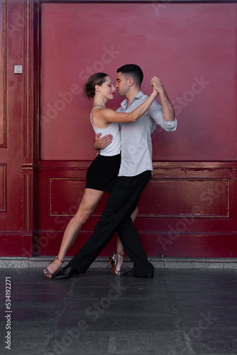 Boy in a suit and girl in shorts and a white t-shirt Couple dancing Tango, with a red background.