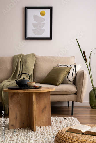 Creative composition of stylish living room with beige sofa  pillow  wooden coffee table  mock up poster frame  black tea pot  vase and elegant decoration. Cozy home decor. Template.