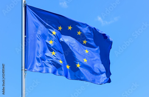 The flag of Europe, the symbol of the European Union and the Council of Europe, is a blue banner with 12 yellow stars forming a circle in the middle on a background of blue sky during the summer day