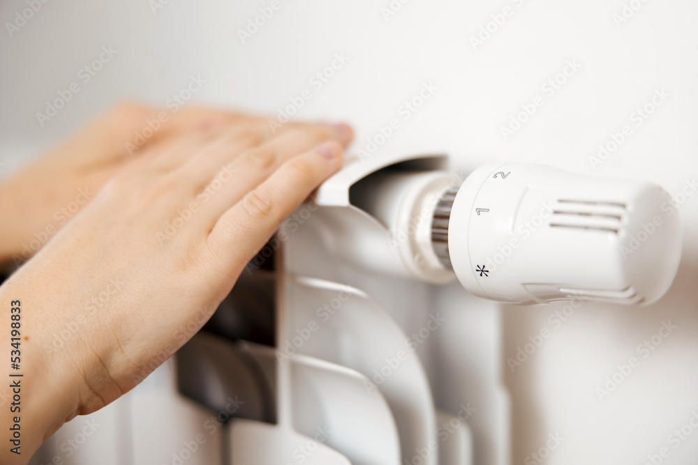 Woman hands on white heating radiator, close up view. It is cold, person warms up. Central heating system. Heating is getting more expensive, save money. Energy crisis. Woman hands on white heating radiator, close up view. It is cold, person warms up. Central heating system. Heating is getting more expensive, save money. Energy crisis.