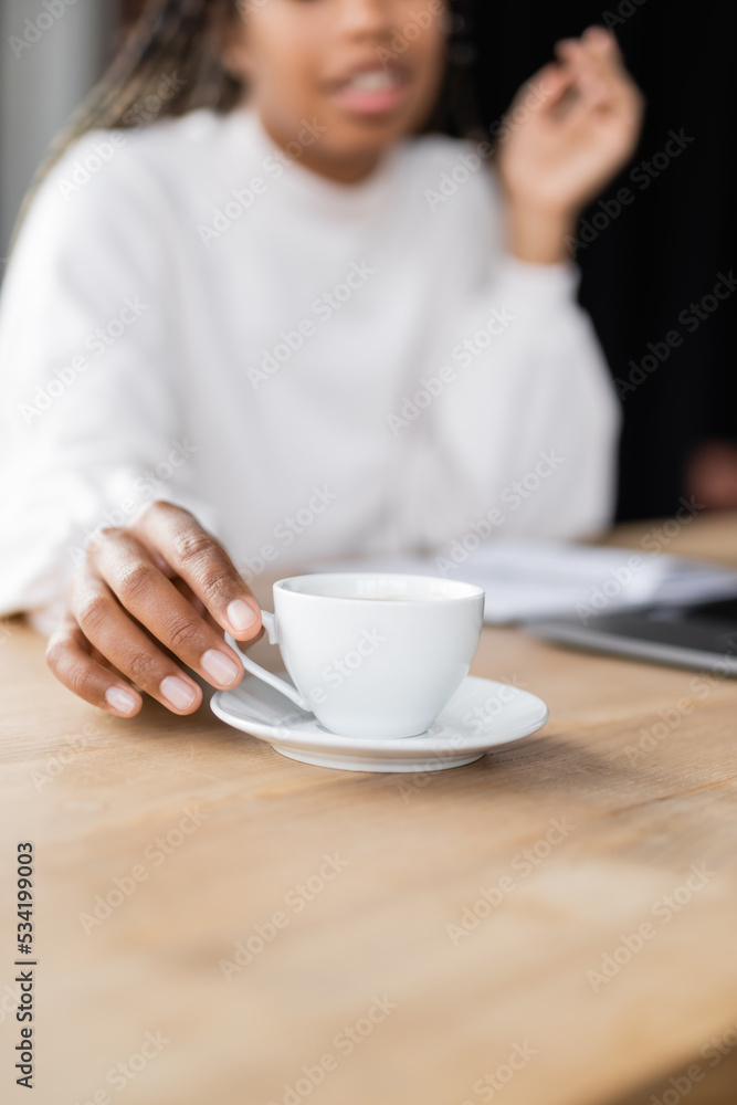 Cropped view of blurred african american businesswoman taking cup of coffee in office. Cropped view of blurred african american businesswoman taking cup of coffee in office.