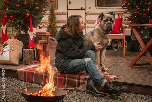 Happy young girl and dog spend time together on Christmas holidays. Cane Corso and his mistress celebrate the New Year in nature near the motor home and by the fire.