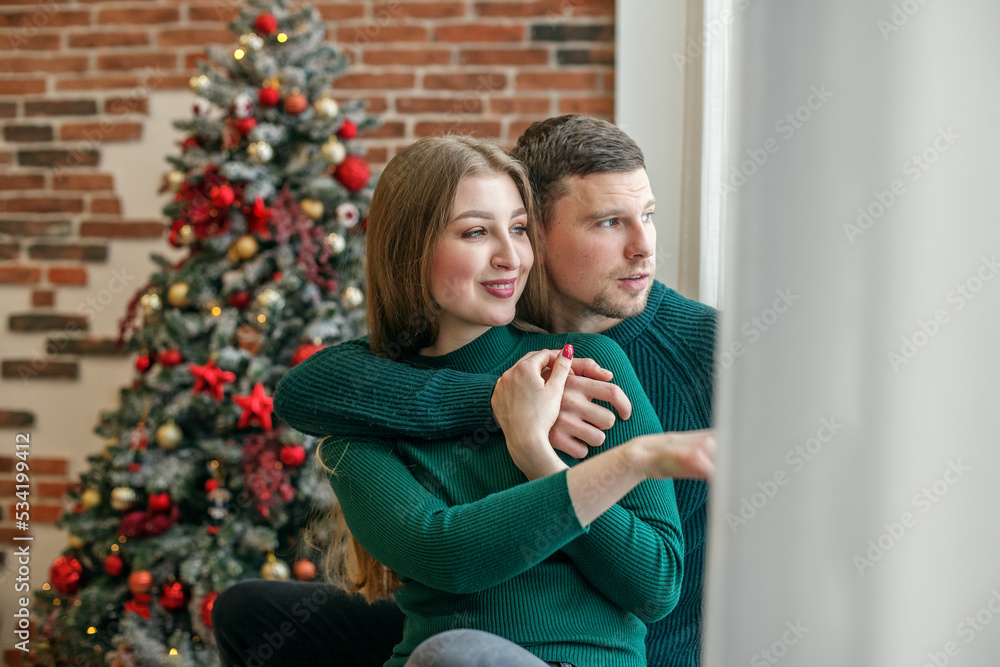 Couple hugging on windowsill and looking out window. Concept of family, Christmas and winter season. Couple hugging on windowsill and looking out window. Concept of family, Christmas and winter season.