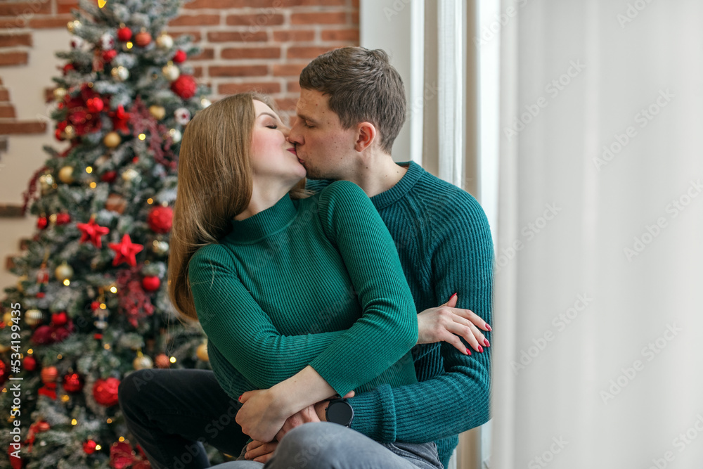Loving couple embrace and kiss on the windowsill. Concept of family, Christmas and winter season Loving couple embrace and kiss on the windowsill. Concept of family, Christmas and winter season
