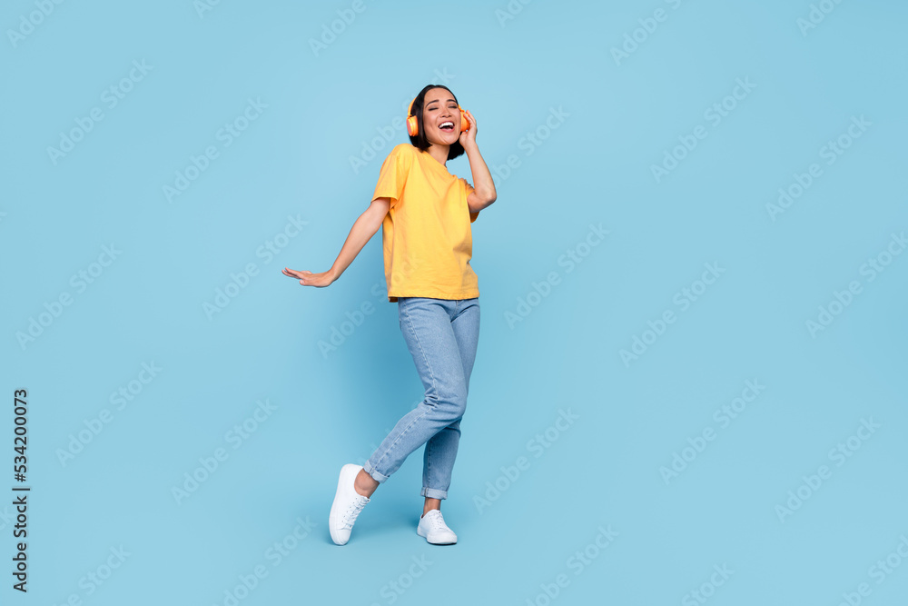 Full length photo of young pretty cute nice korean girl listening music headphones wireless dreamy empty space shopping offer isolated on blue color background Full length photo of young pretty cute nice korean girl listening music headphones wireless dreamy empty space shopping offer isolated on blue color background