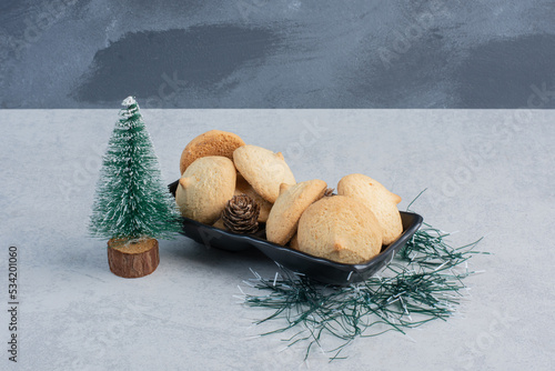 Tree figurine next to a pile of cookeis in a black platter on marble background