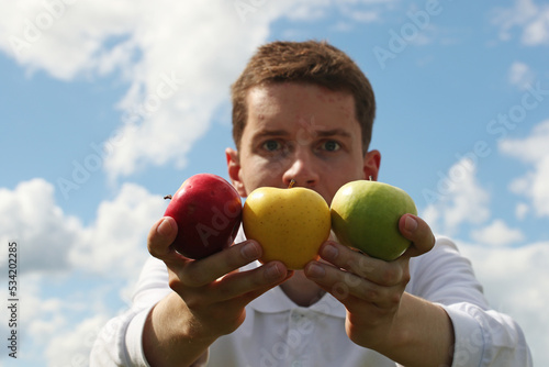 Young man with colourful apples in hands on a blue sky background. Pavel, colourful apples in my hands and sky. Photo was taken 16 July 2022 year, MSK time in Russia.