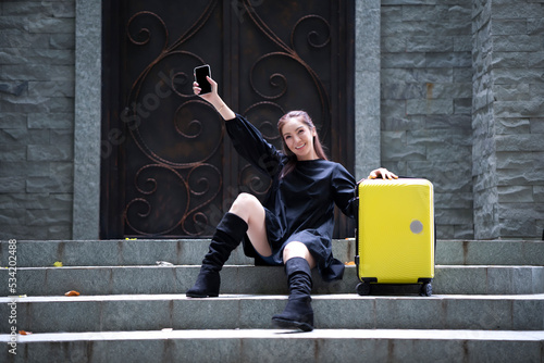 Obraz na plátně Young beautiful woman sit on stair outside the accommodation with yellow luggage