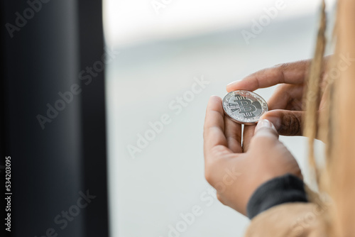 Cropped view of african american businesswoman holding silver bitcoin in office.