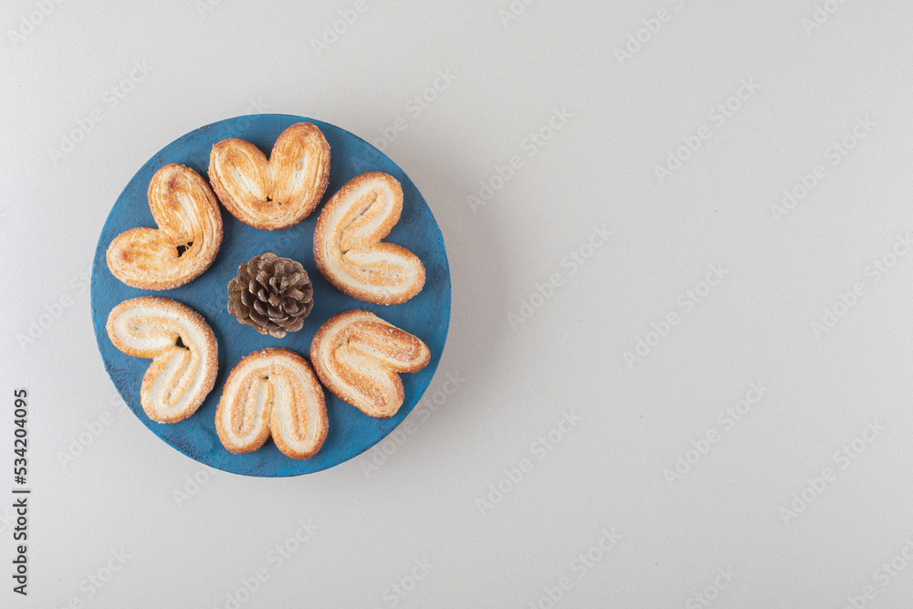 Pine cone surrounded by flaky cookies on a platter on marble background Pine cone surrounded by flaky cookies on a platter on marble background